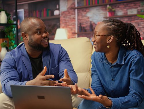 African american young freelancers on couch sharing a business idea African american young freelancers on couch sharing a business idea, using modern technology and tools to analyze trends and boost success. Couple improving workflow efficiently. Camera A.