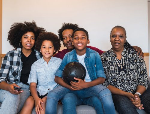 Multi-generation family watching soccer match at home. Happy african american multi-generation family watching soccer match on television in living room at home. Family and sport concept.